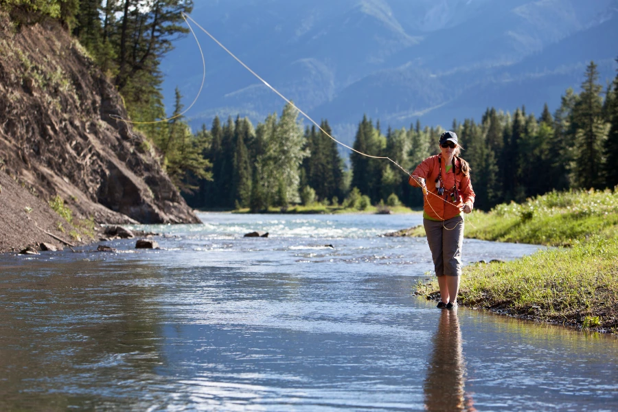 Flugfiskare kastar med flugspö i en klar älv omgiven av skog och berg.