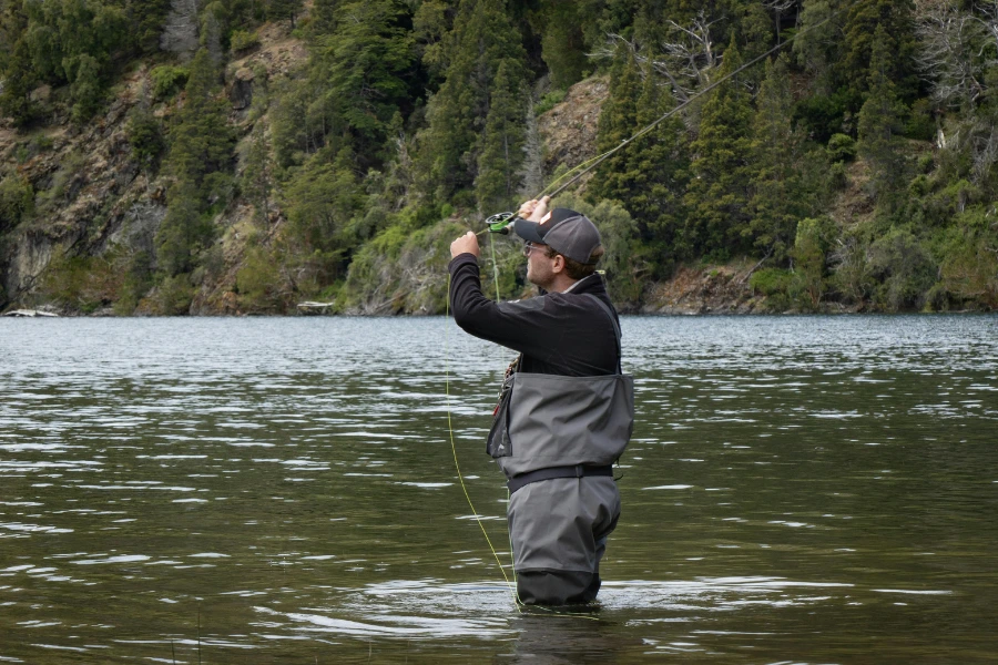 Flugfiskare i vadarbyxor kastar med flugspö i en sjö omgiven av skog.